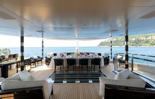 Overview of the aft deck onboard charter yacht SARASTAR, sofas arranged in the foreground facing each other with alfresco dining area in the background