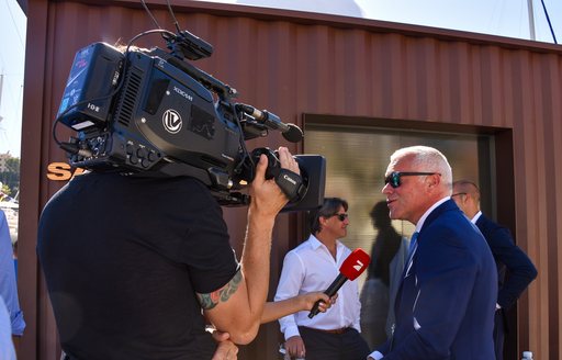 Man with film camera speaking to interviewee at Monaco Yacht Show 2018