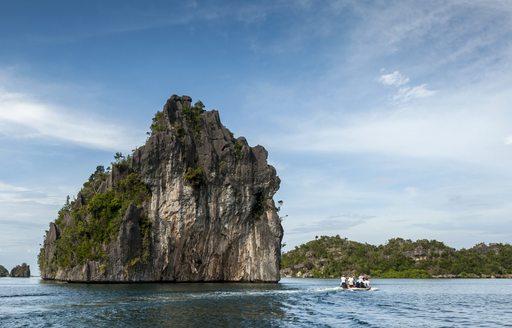 people observing large rock formation from a small boat in raja ampat islands