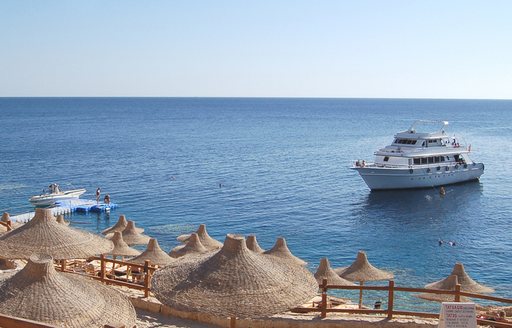 Motor yacht charter in bay with parasols on beach