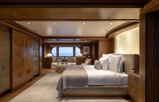 Overview of the master cabin onboard charter yacht TREEHOUSE, central berth facing port with a large window and seating area in the background.