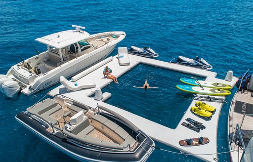 Selection of water toys deployed adjacent to charter yacht NITA K II, with two charter guests enjoying the sun