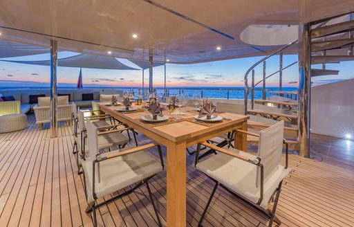 Alfresco dining area onboard charter yacht BIG SKY, long table surrounded by cream director's chairs
