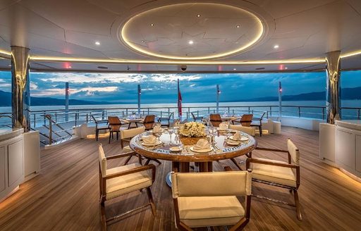 Overview of the aft main deck onboard charter yacht ELEMENTS, with alfresco dining set up in the foreground and seating in the background
