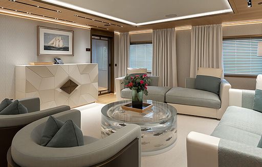 Private lounge area in a master cabin onboard charter yacht LA DATCHA. Neutral colored sofas and armchairs face in towards a see-through coffee table