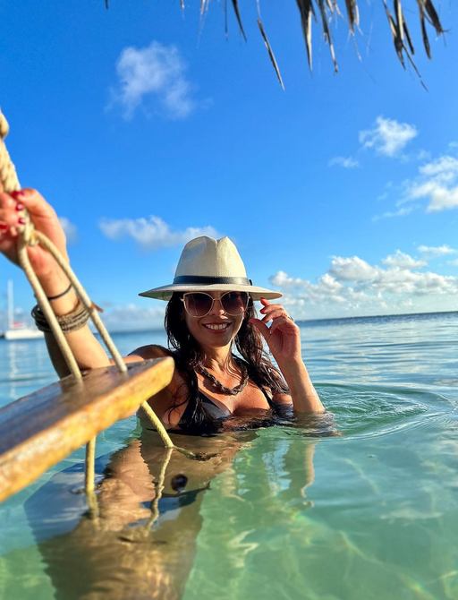 Woman in hat floating next to a beach swing with boat in the distance 