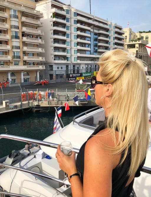 A lady with champagne on board a charter yacht watches the cars race by at the Monaco Grand Prix