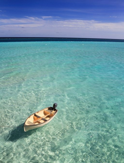 a wooden rowing boat floats in the deserted crystal clear waters of the Maldives