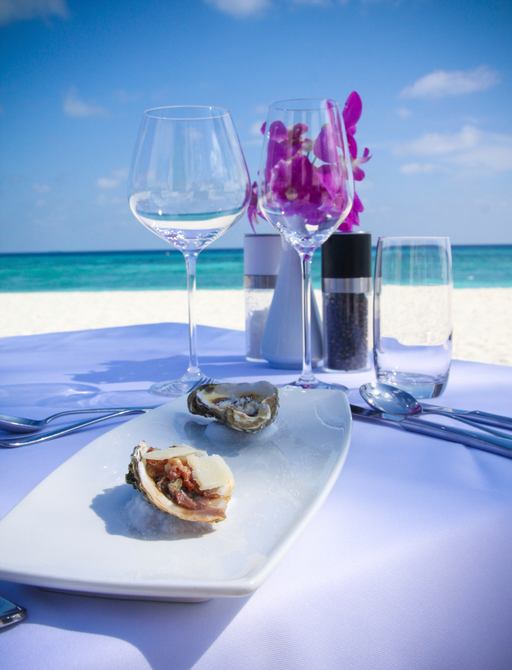 a table set with glasses and dish of food on a beach in the maldives
