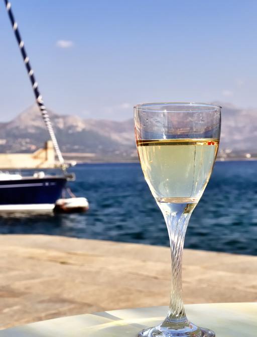 A glass of white wine with the bow of a sail yacht and mountains in the distance