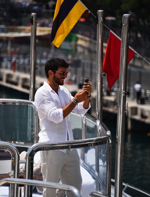 A smiling man takes photos from his mobile on board a yacht trackside at the Monaco Grand Prix