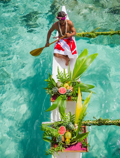 A local paddles a kayak filled with beautiful arranged fruit baskets in Tahiti