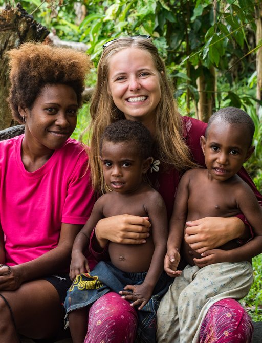 A smiling tourist sits with some local children in the Solomon Islands