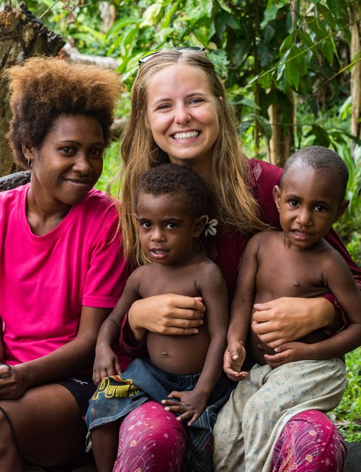 A smiling traveller sits with some local children in the Solomon Islands