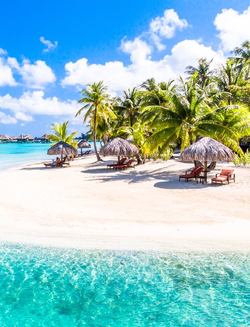 Small island Tahiti with crystal blue waters, soft white sand and straw umbrellas with sun loungers