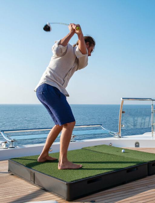 A man swings a golf club from a tee onboard MY Sunrays